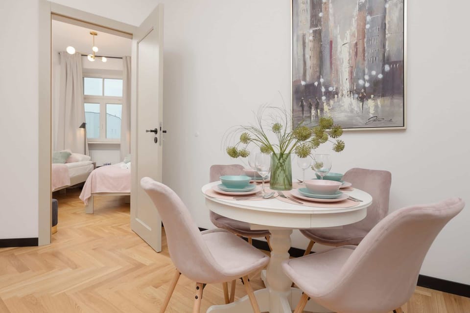 A dining area featuring pastel pink chairs, a round table, and modern wall art for a cozy ambiance.
