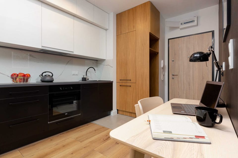 A modern kitchen with black cabinets and white countertops. A table with chairs is visible in the background.