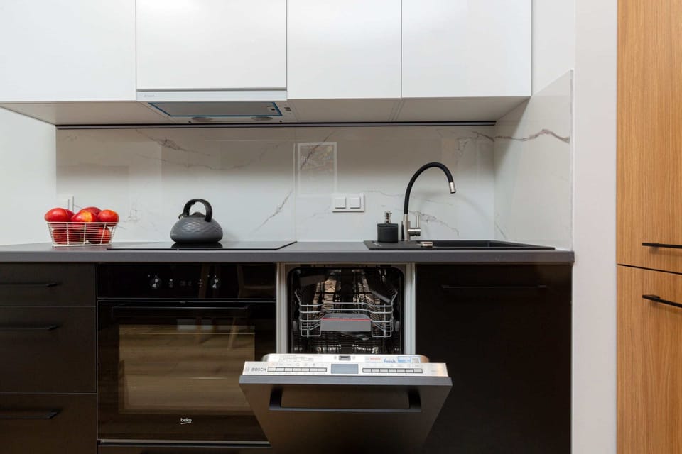 A modern kitchen with black cabinets and white countertops. A table with chairs is visible in the background.