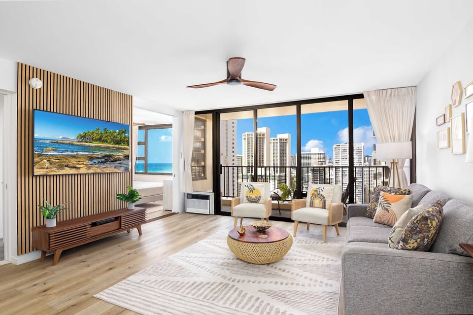 Bright living area w/ floor-to-ceiling windows & balcony access showcasing ocean & city views