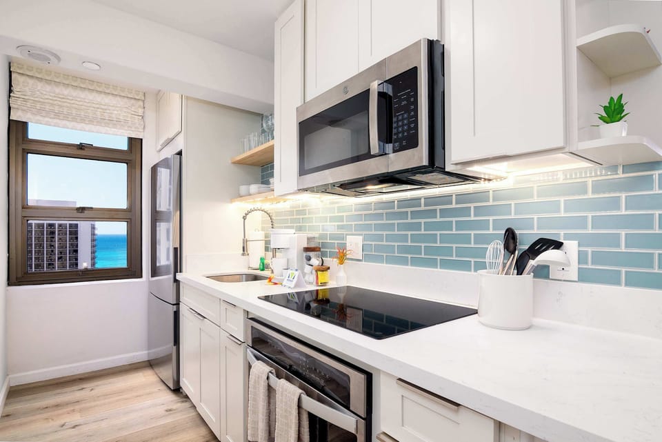 Sleek galley kitchen w/ modern appliances, tile backsplash & window views