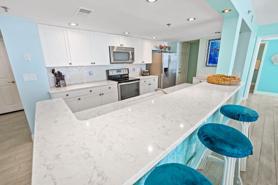 Your spacious kitchen features white quartz counters, stainless appliances, and cheerful turquoise accents that create the perfect backdrop for vacation meal prep.