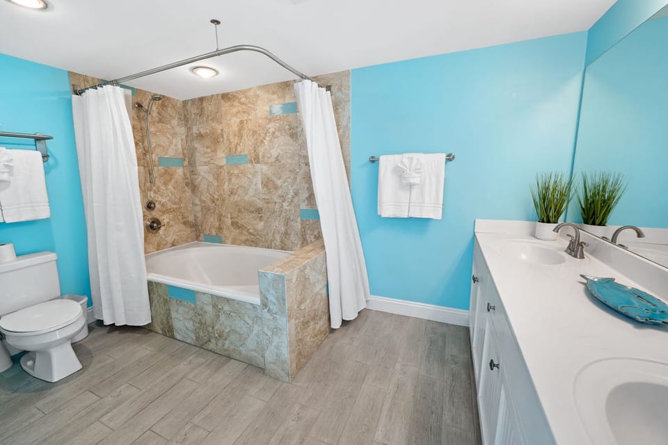 Your private spa-like bathroom awaits with a luxurious soaking tub, elegant marble surround, and calming turquoise walls.