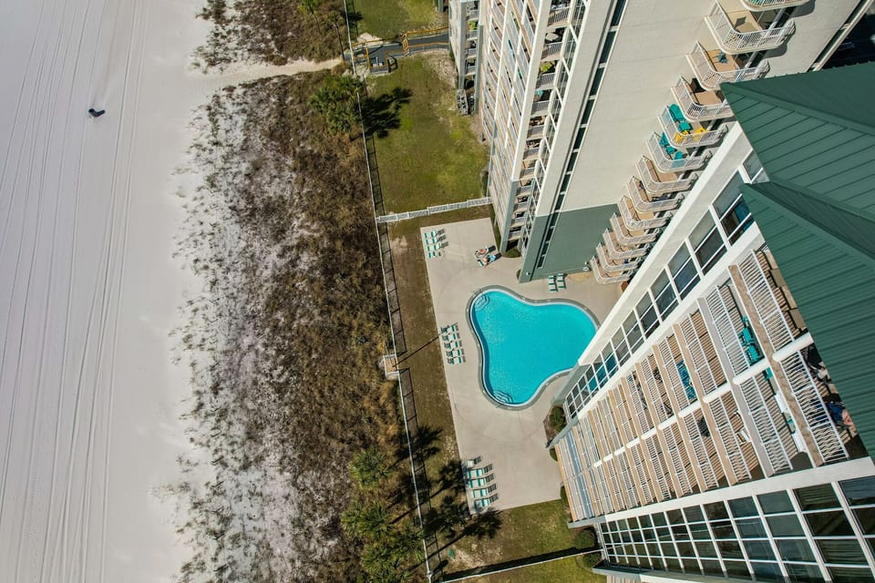 Beachfront property featuring a kidney-shaped pool surrounded by multi-story buildings with balconies, directly adjacent to pristine sandy beach.