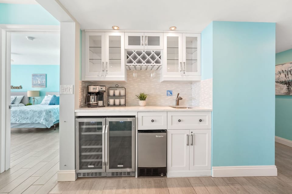 Your elegant kitchenette features white cabinetry, wine cooler, and coastal charm with soothing blue accents throughout your beachside retreat.
