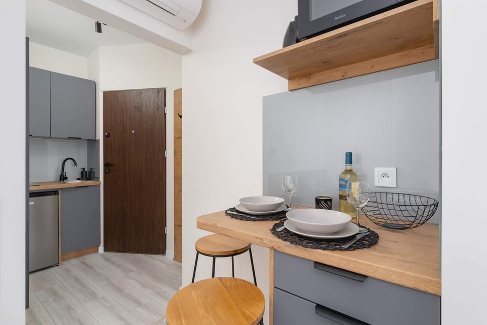 A compact dining area with a round table, wooden chairs, and a stylish kitchenette in the background.
