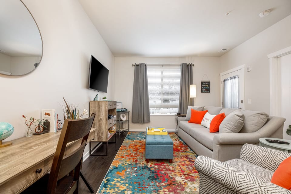 Bright living area w/ plush sofa, colorful rug & TV, flowing into a cozy dining space by the window.
