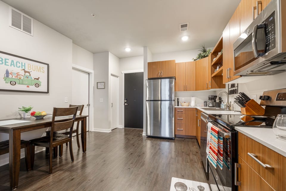 Open kitchen w/ stainless steel appliances, wood cabinets & dining table for easy meals at home.