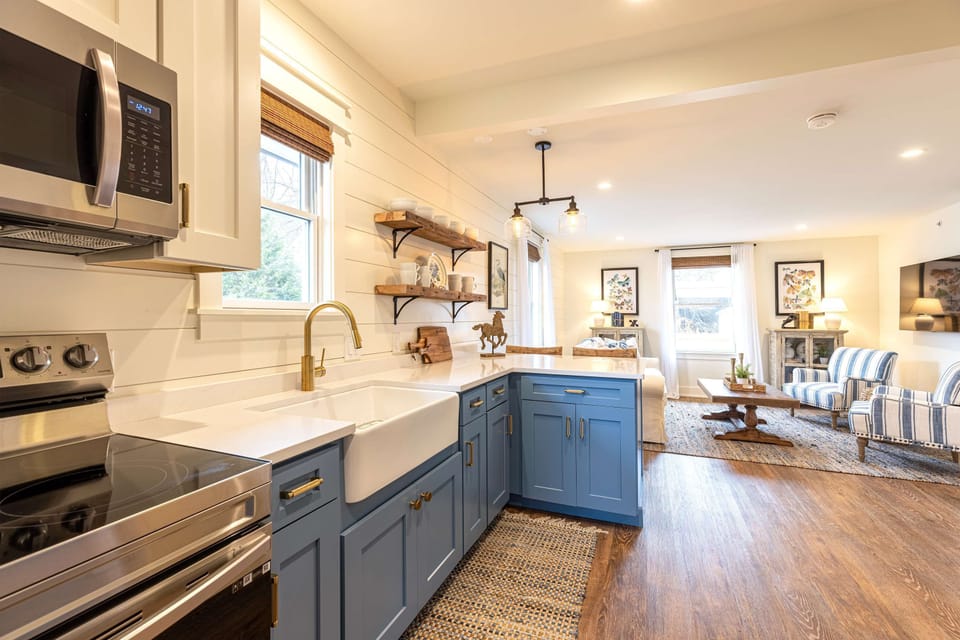 A full kitchen with a blue island and farmhouse sink -  designed for those who love to settle in.