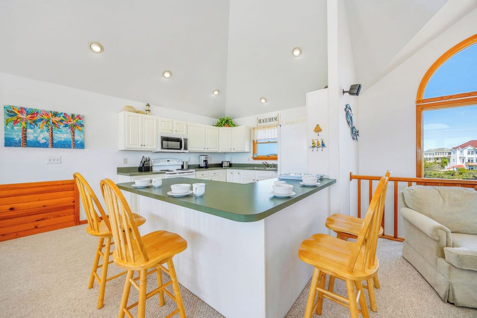 Gather around the welcoming breakfast bar in your bright, open kitchen, where cheerful wood seating and coastal decor set a relaxed tone for morning coffee or evening meals.