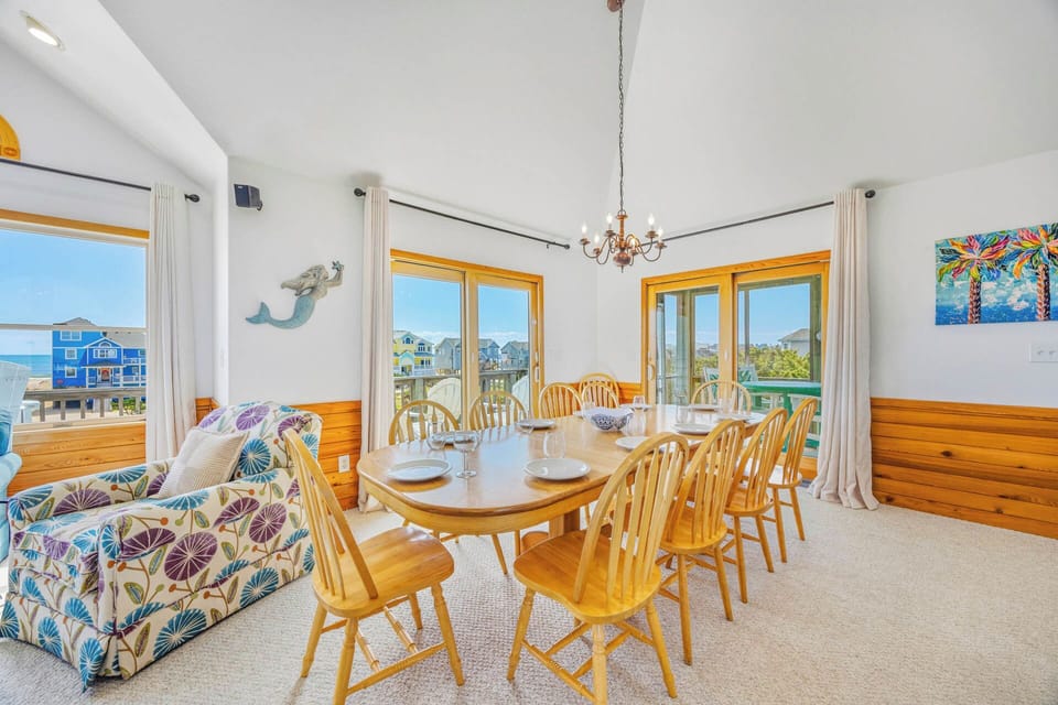 Gather around this spacious dining table where your group can share meals and stories while soaking in coastal views through multiple windows that frame the ocean and surrounding area.