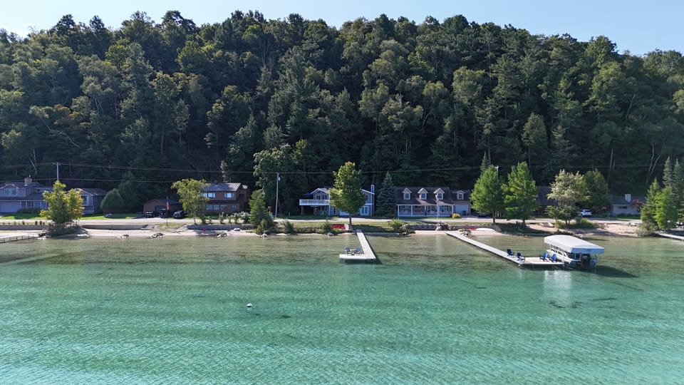 OVERVIEW:  Aerial view from over Crystal Lake of the cottage, dock, and bonfire ring, with the mooring buoy for the property also shown in the photo.