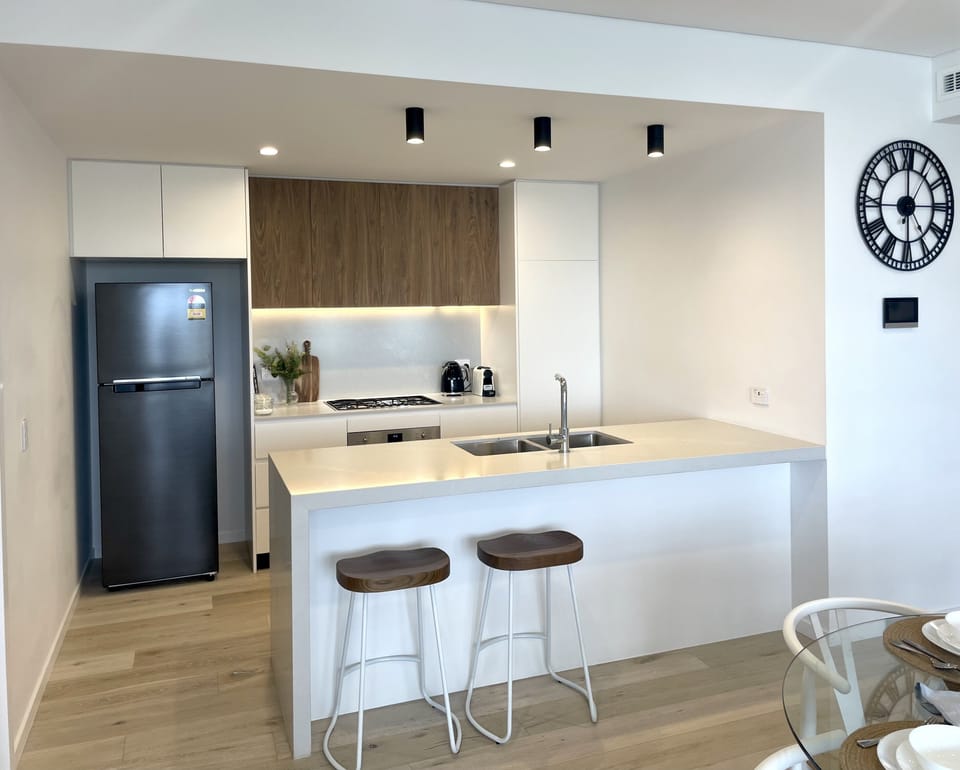 Open plan kitchen with two stools equipped with oven, gas cook top, microwave 