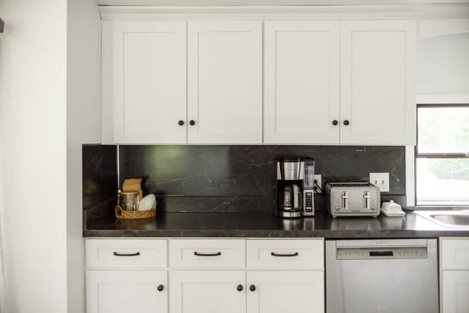 Coffee maker on counter with the upper cabinets on the left side stocked with coffee grounds & tea packets.