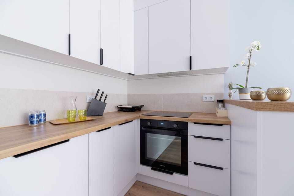 A sleek kitchen with white cabinets, a built-in oven, and a wooden countertop.
