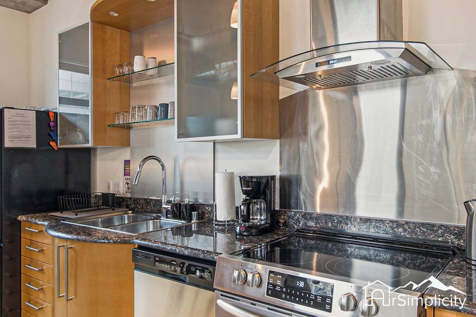 - Prep your meals with ease at this modern setup with deep sink and glass cooktop
- Open cabinets display dishes and glasses for added convenience
- Coffee maker, oven, and dishwasher make this kitchen as practical as it is sleek