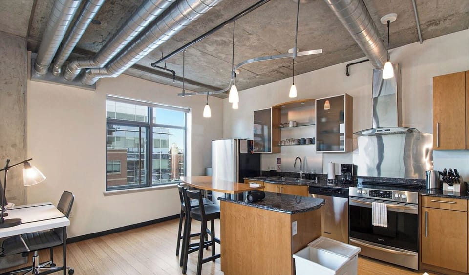 - Bright and stylish kitchen with an island for morning coffee or casual meals
- Pendant lights and exposed ductwork enhance the industrial chic design
- Large window fills the space with natural light and city views