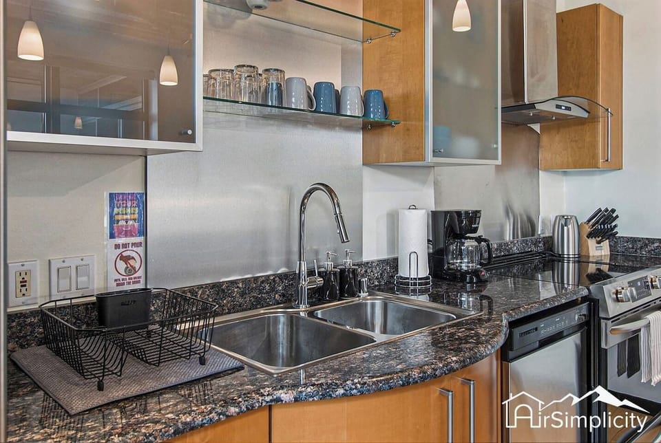 - Double sink and granite countertops make meal prep and cleanup stylish and simple
- Open shelving keeps cups and dishes within easy reach for a streamlined setup
- Sleek design paired with modern fixtures adds to the industrial flair
