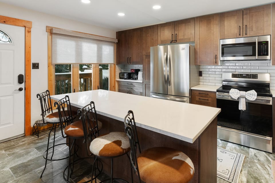 Kitchen next to the main entryway.  Granite island bar with seating for 4. stainless steel appliances in the background.