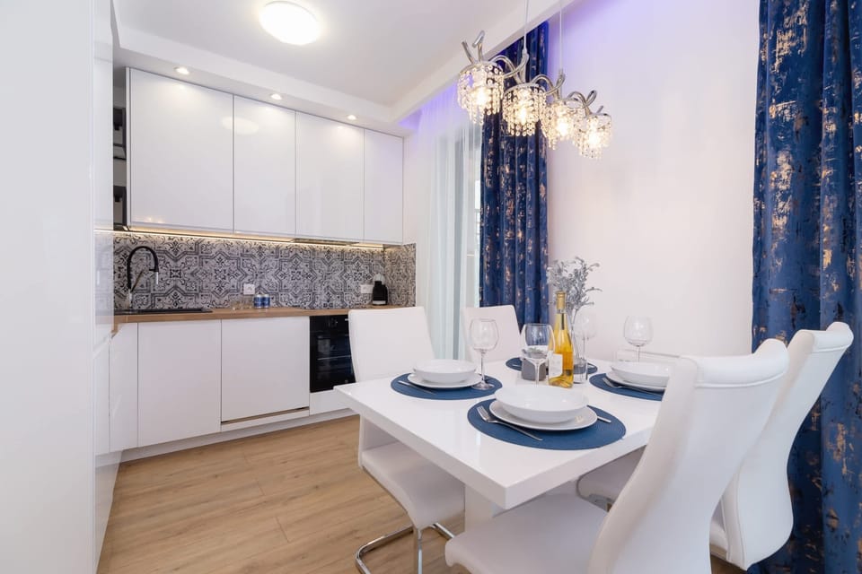A compact dining and kitchen area with white chairs and a sparkling chandelier.
