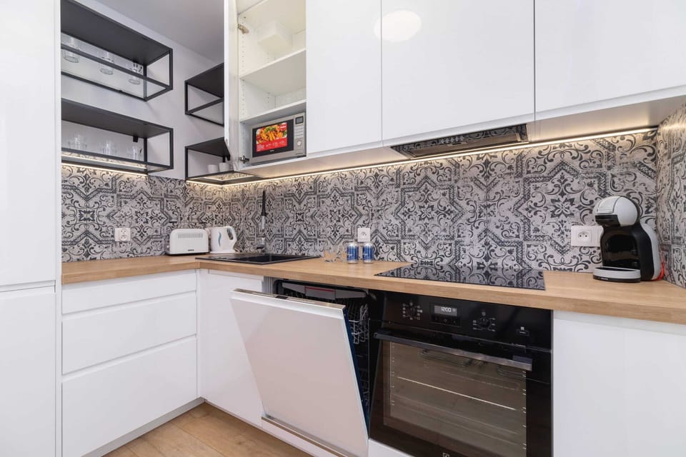 A modern kitchen with white cabinets, patterned backsplash tiles, and built-in appliances.

