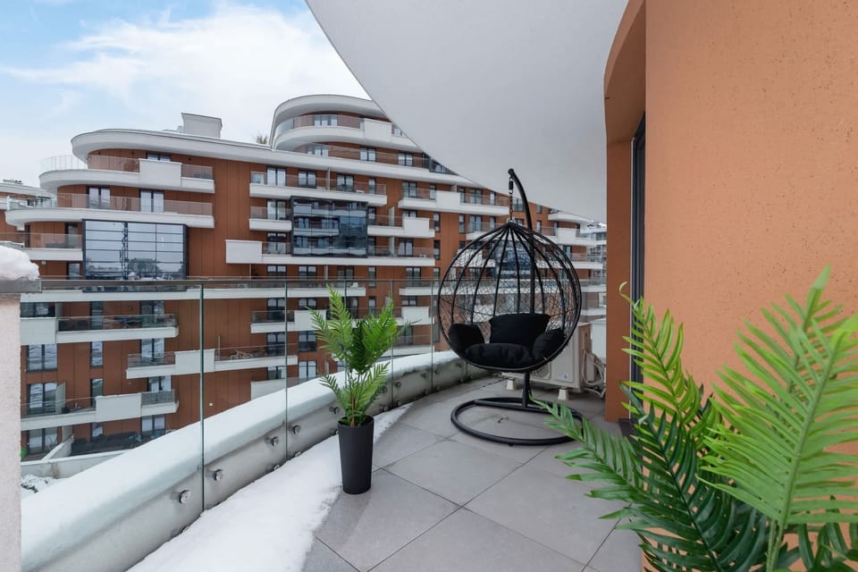A balcony with outdoor seating and views of modern architecture and greenery.
