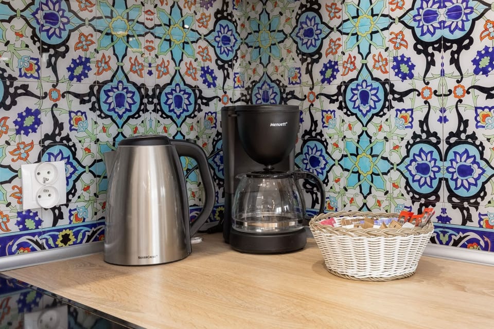 A close-up of a coffee station with patterned tiles, a kettle, and mugs, adding a homely touch.
