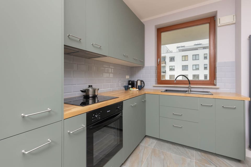 A kitchen with sleek green cabinets, wooden countertops, and a large window for natural light.
