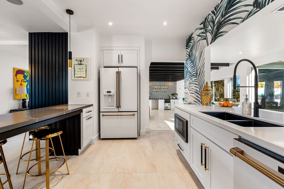 Bright designer kitchen - French door fridge with gold handles, black granite breakfast bar, gold stools and bold pop-art wall accent.