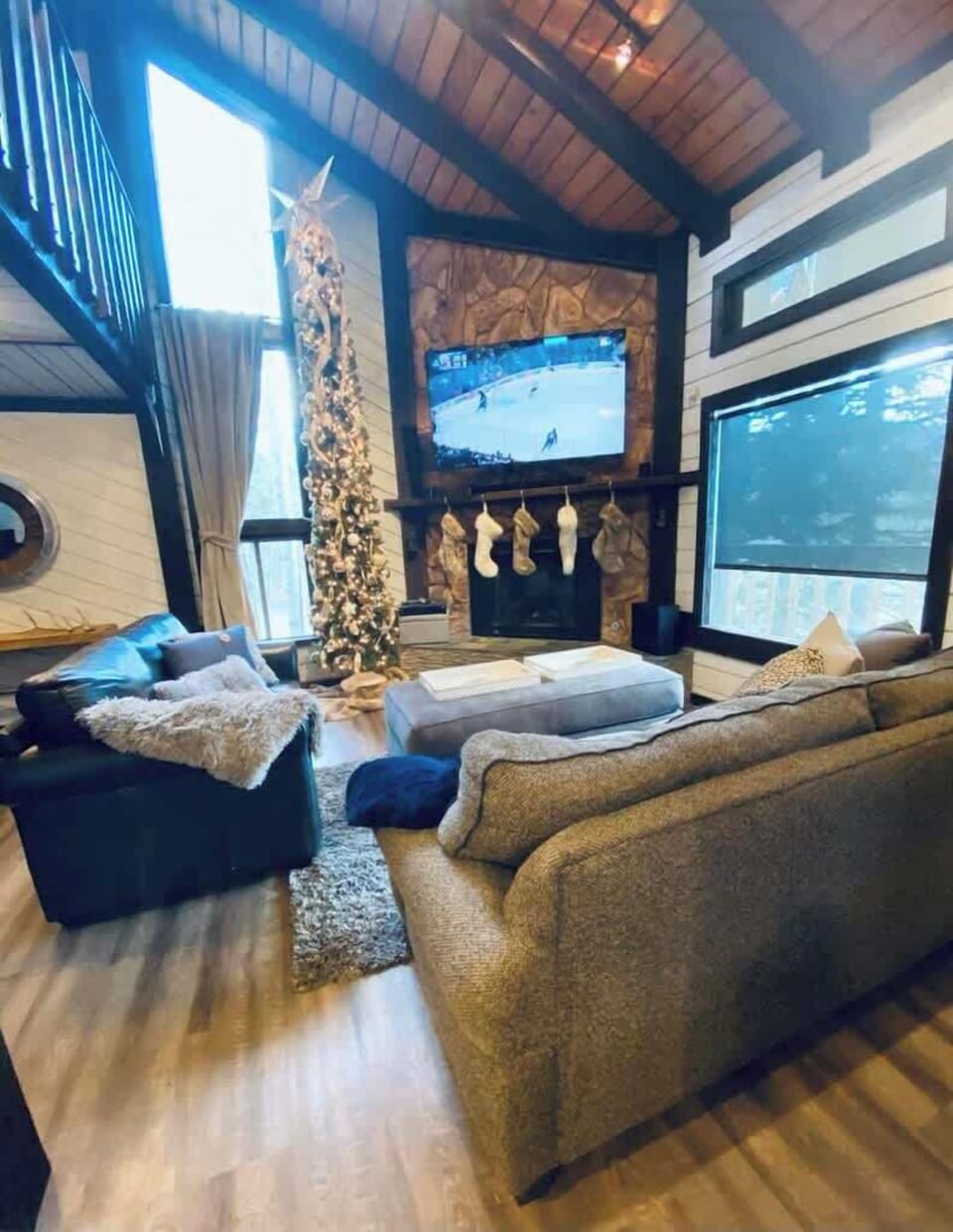 Enjoy the perfect blend of comfort and style with a plush seating area and a grand Christmas tree adding festive charm. The stone fireplace and expansive windows let in natural light, enhancing the cozy ambiance.