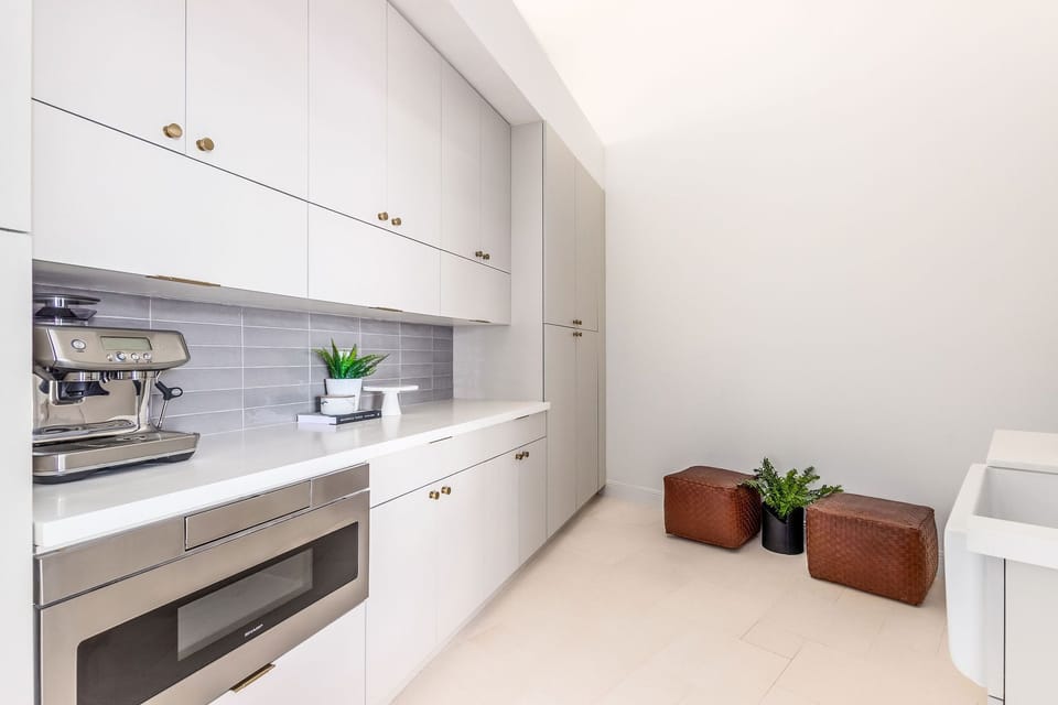 A sleek secondary kitchen space designed for convenience, featuring clean white cabinetry, built-in appliances, and a bright, minimalist layout that makes prepping meals effortless.