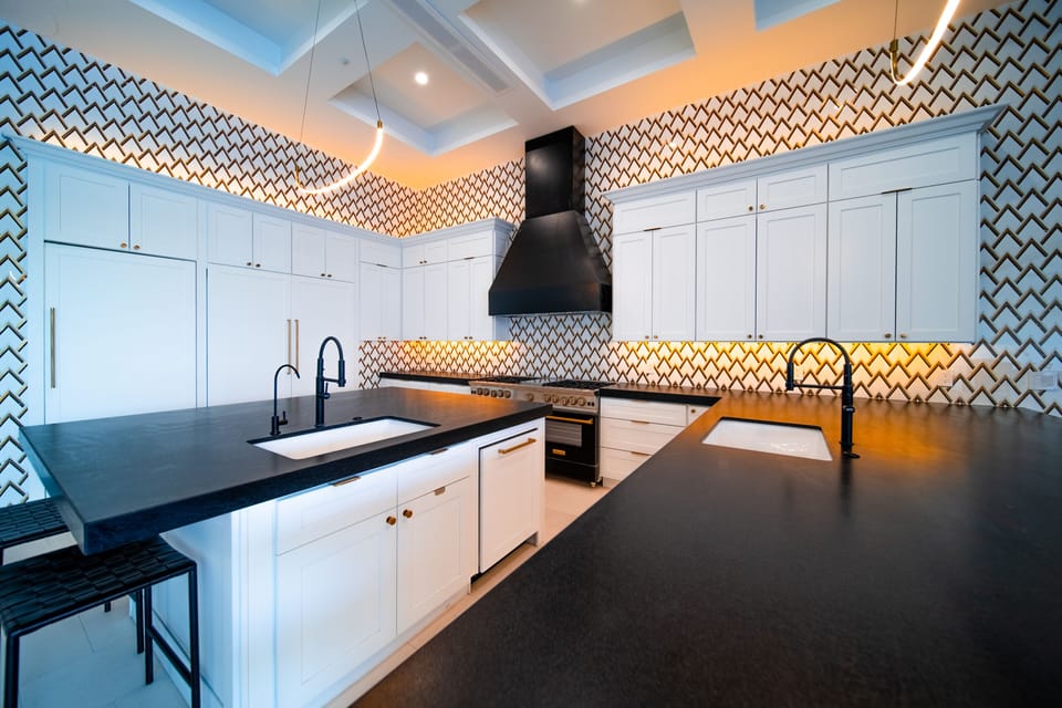 A spacious modern kitchen with sleek white cabinetry, bold black countertops, and a striking patterned backsplash. Plenty of room to cook, gather, and entertain around the oversized island.