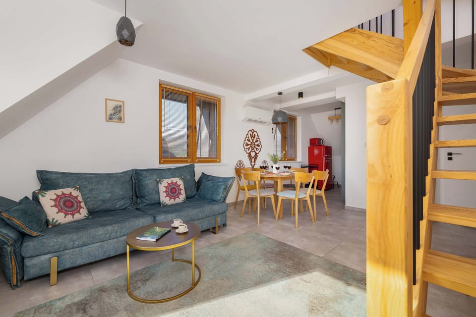 A spacious living and dining area with a sofa, wooden furniture, and a staircase leading upstairs.