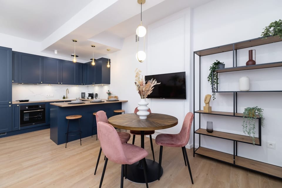 A dining area with pink chairs, a round table, and decorative shelves.
