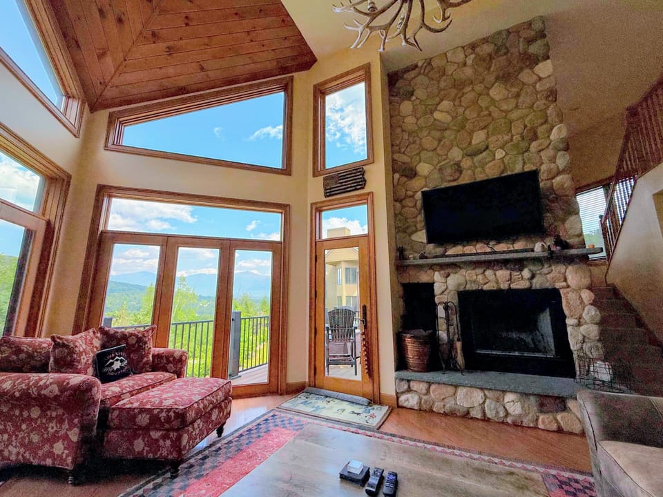 This retreat features vaulted ceilings, expansive windows showcasing breathtaking views of the Presidential Range and Mount Washington, and a stunning floor-to-ceiling river rock wood-burning fireplace.