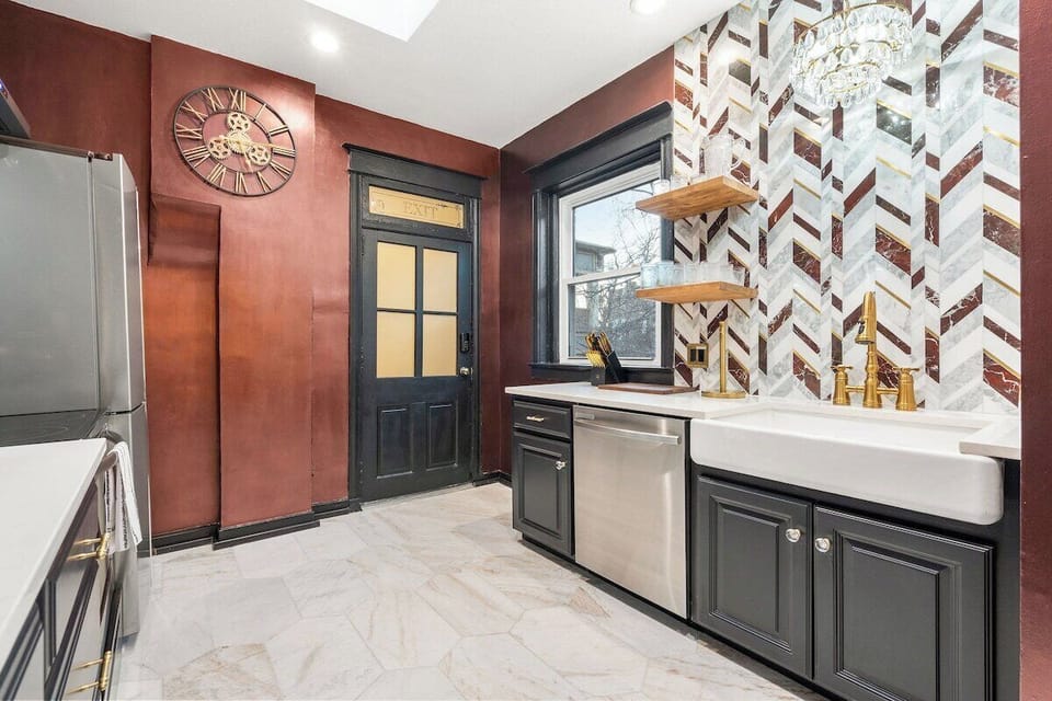 A striking farmhouse sink, brass fixtures, and dramatic herringbone backsplash create a memorable blend of modern luxury and vintage speakeasy charm. There is also a private rear entrance off the kitchen which leads to the back of the home.