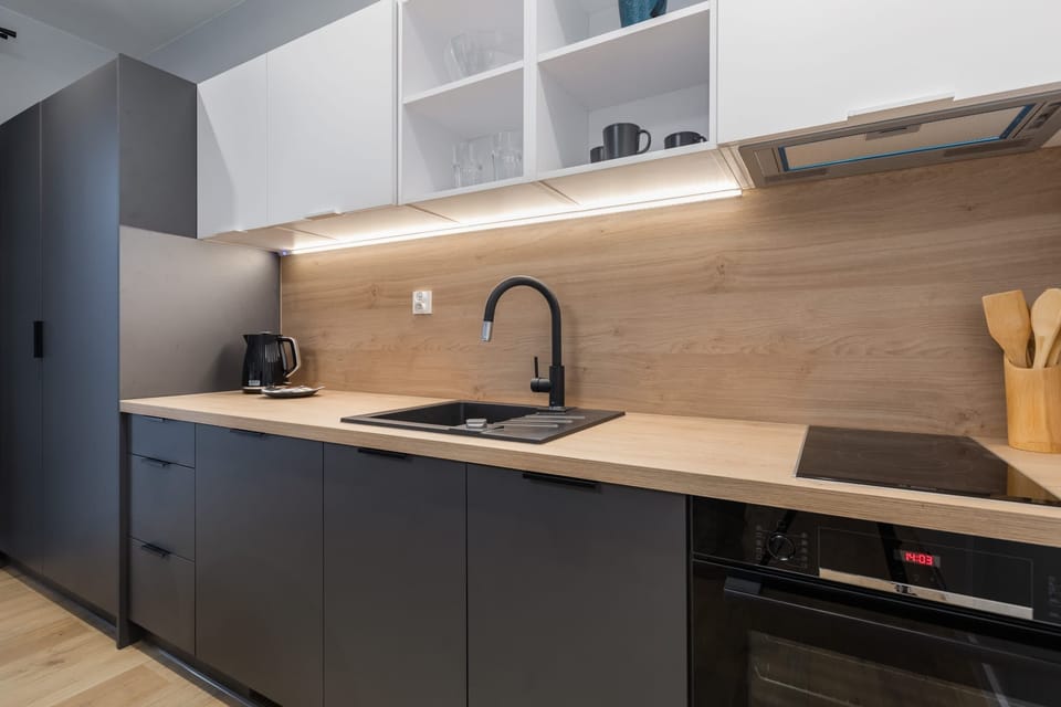 Compact kitchen with dark cabinetry and wooden countertops, featuring modern appliances.
