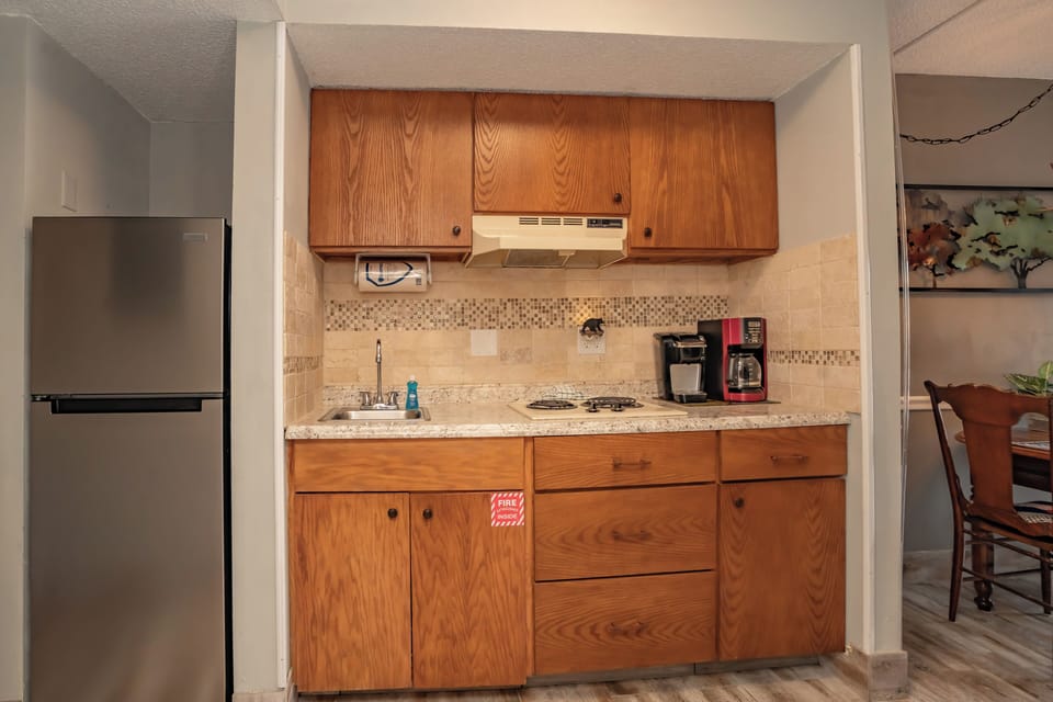 Your compact kitchenette features warm wood cabinetry, a full-size refrigerator, stovetop, sink, and a coffee maker ready for your morning brew—everything you need to feel at home.