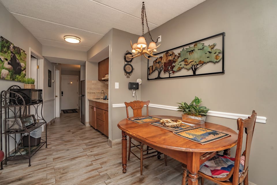 Gather around the charming wooden dining table, set with rustic placemats and warmed by a unique antler chandelier overhead. The cozy space opens to your fully-equipped kitchenette, ready for easy meal prep.