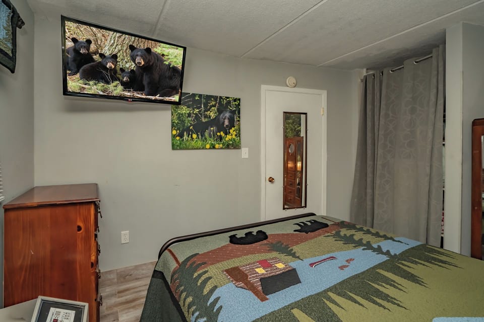 Your cozy bedroom features rustic wood furnishings and a wall-mounted TV for your entertainment. Natural light filters through curtained windows, creating a warm and peaceful retreat after your mountain adventures.