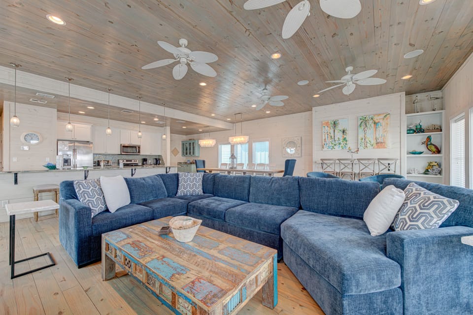 Relax on your plush sectional sofa beneath stunning wood ceilings with gentle ceiling fans keeping you cool in this coastal haven.