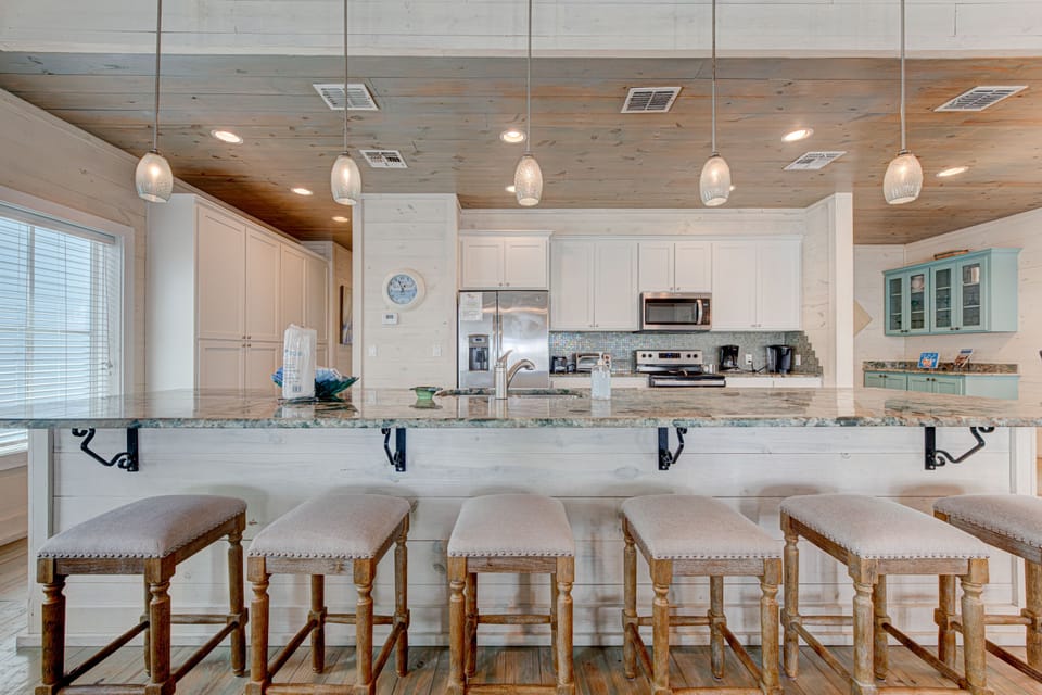 Gather around this stunning granite island where coastal-inspired pendant lights illuminate your culinary adventures and morning coffee conversations.