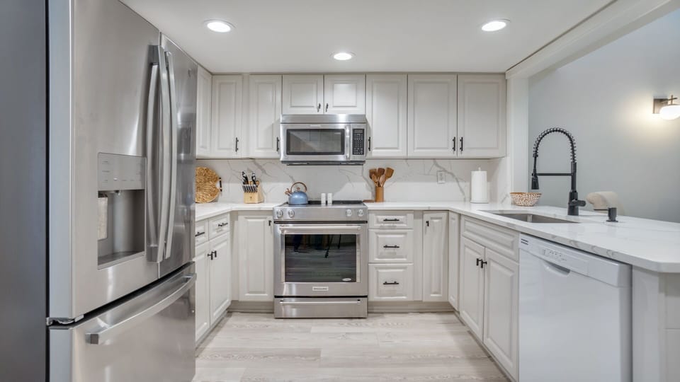 Clean white cabinetry offers generous storage, paired with stainless steel appliances including a full-size refrigerator, range, and microwave.