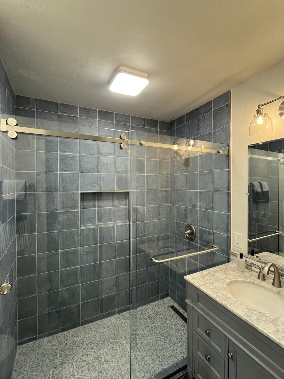 The en suite bathroom is attached to the primary bedroom. It features a an extra large tiled walk in shower with barn door style sliding glass doors, a toilet, and a marble-topped vanity.