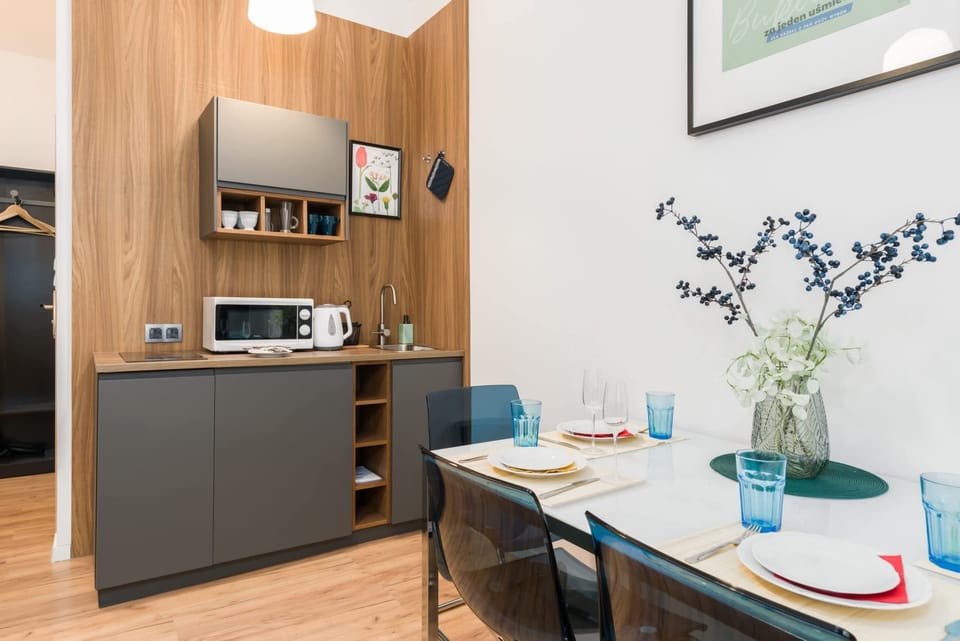 A modern kitchenette with wooden cabinetry, sleek appliances, and a dining table nearby.
