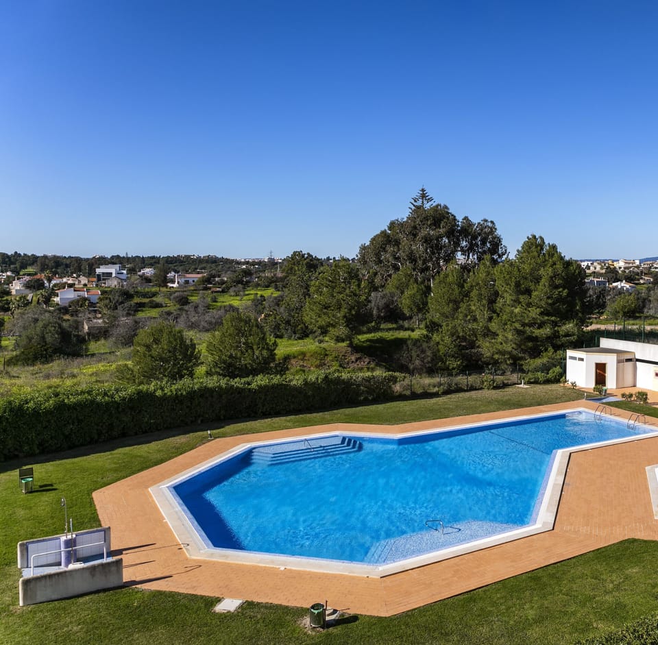 Large communal swimming pool at Apartment Mar a Vista with spacious sun terrace, lush green landscaping, and panoramic views across the Algarve countryside, perfect for relaxing on warm sunny days