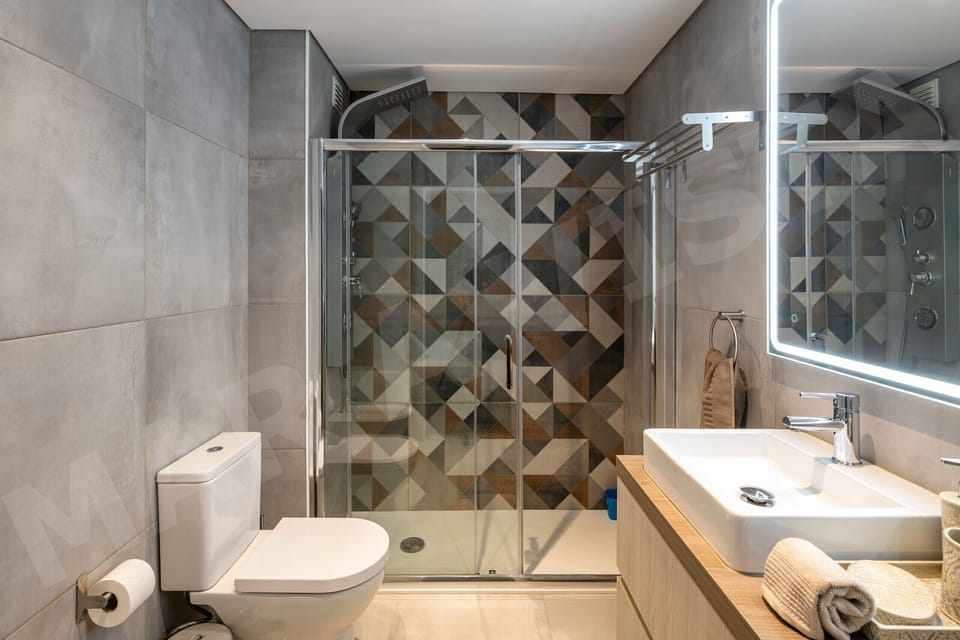 Modern bathroom in Apartment Mar a Vista featuring stylish geometric patterned tiles, a spacious walk-in shower with glass screen, white WC, and contemporary wall-mounted basin, finished to a high standard