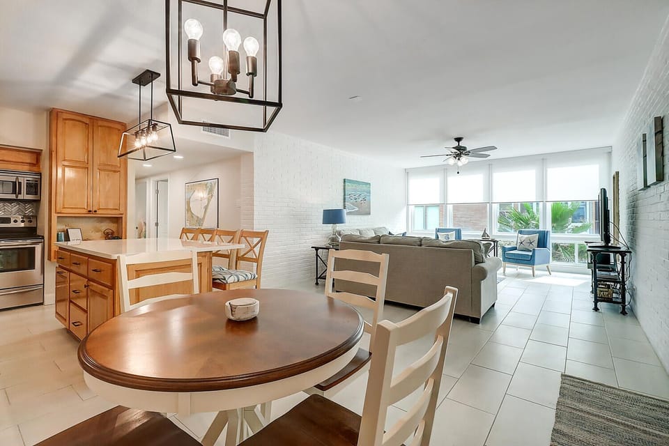 Your open-concept haven flows seamlessly from kitchen to living room, where natural light streams through floor-to-ceiling windows onto stylish modern furnishings.