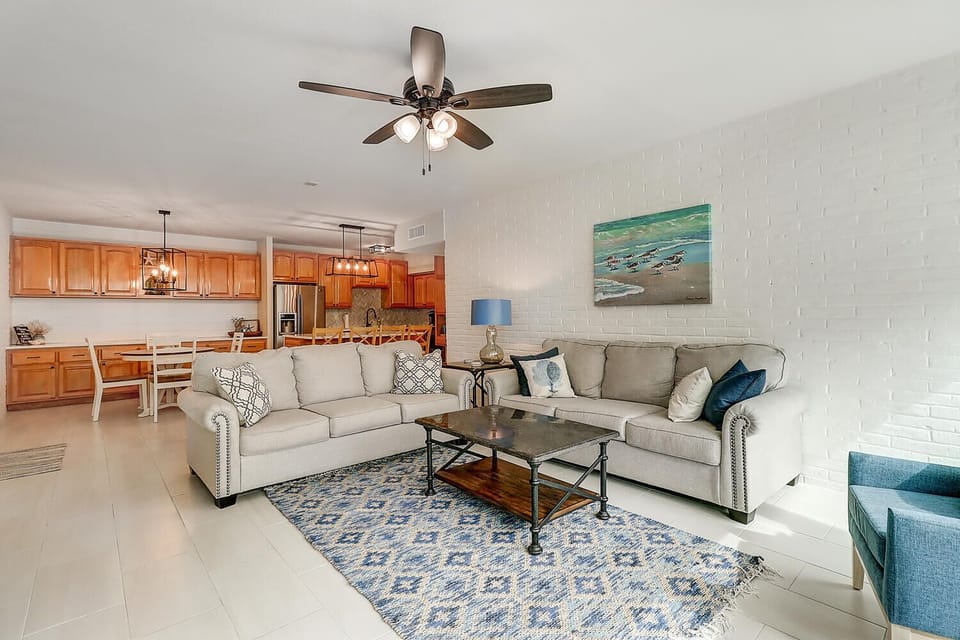 Relax in your spacious open-concept living area with comfortable sectional seating, coastal artwork, and a fully equipped kitchen perfect for preparing meals together.