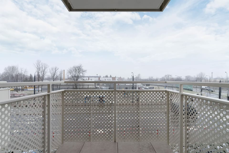 A balcony with a metal railing and a view of the surrounding greenery and open sky.
